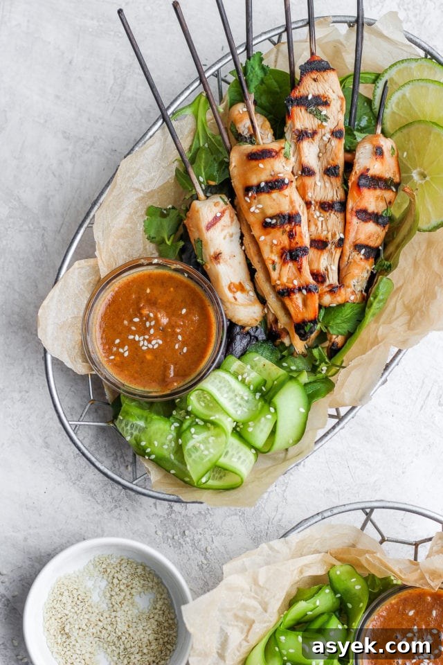 Grilled Thai chicken skewers in a wire basket with strips of cucumber and a small dish of dressing.