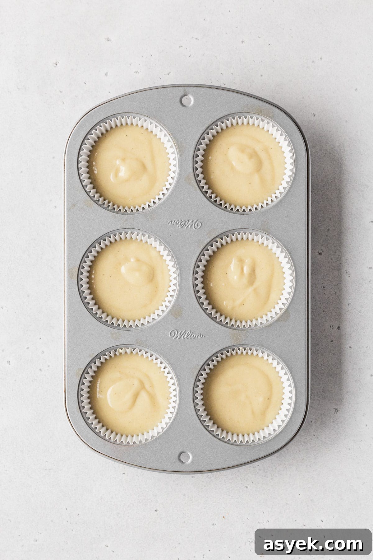 Muffin tin filled with white paper liners and dairy-free vanilla cupcake batter before baking.