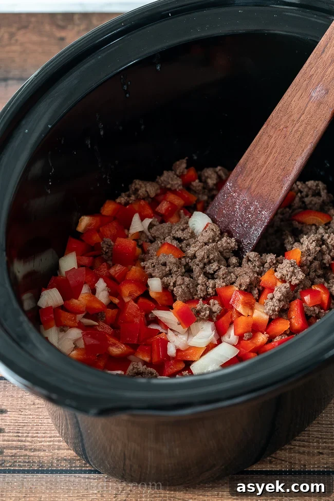 Homemade Chili Recipe from Scratch - Authentic Chili Con Carne 3 Black slow cooker filled with ground beef, red bell peppers and onions for making chili.