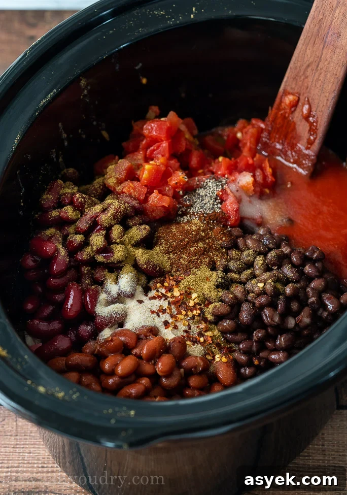 Homemade Chili Recipe from Scratch - Authentic Chili Con Carne 4 canned beans with ground beef and spices in slow cooker, ready to mix with wooden spoon.