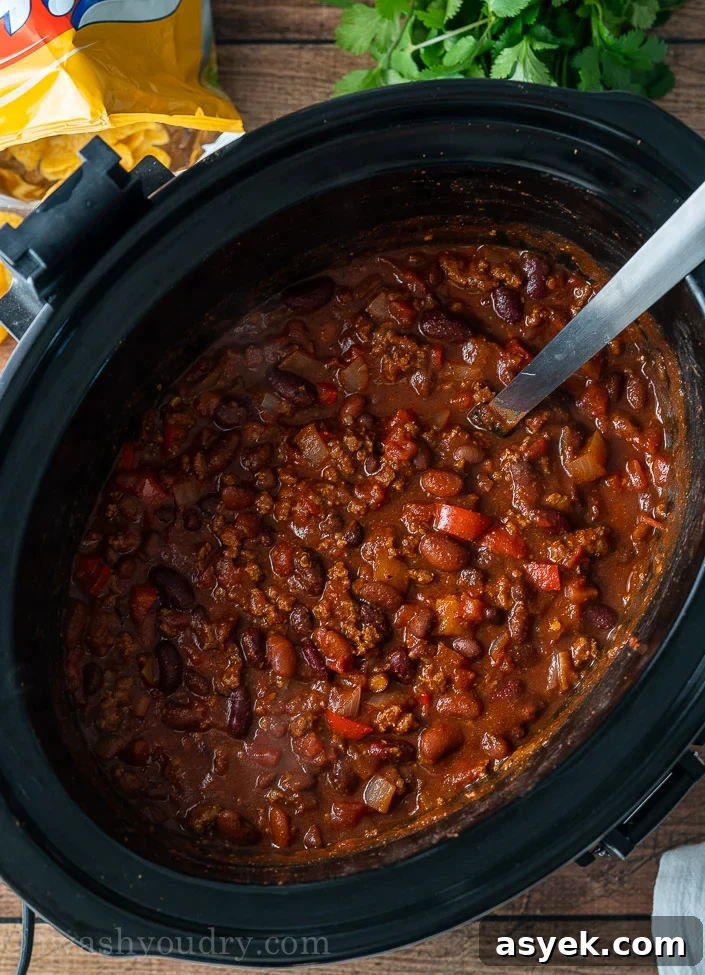 Homemade Chili Recipe from Scratch - Authentic Chili Con Carne 5 black slow cooker with chili inside with spoon and frito chips beside it.