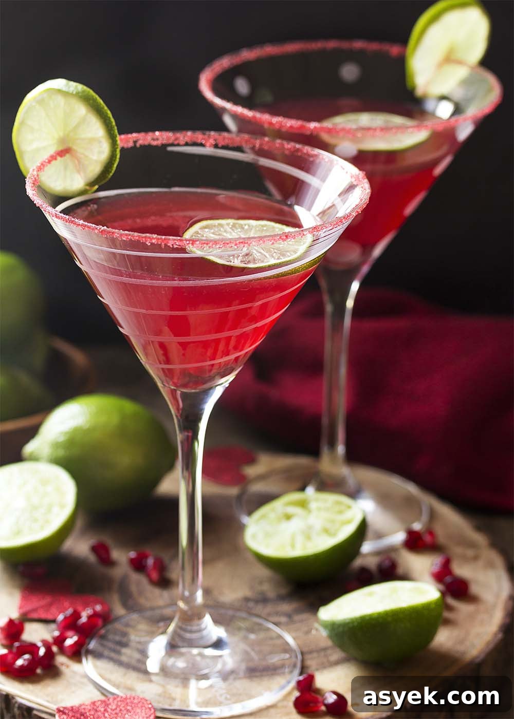 Pomegranate Vodka Martini Recipe: Classic Cocktail 2 Two glasses of pomegranate martini with limes, pom arils, and red hearts around.