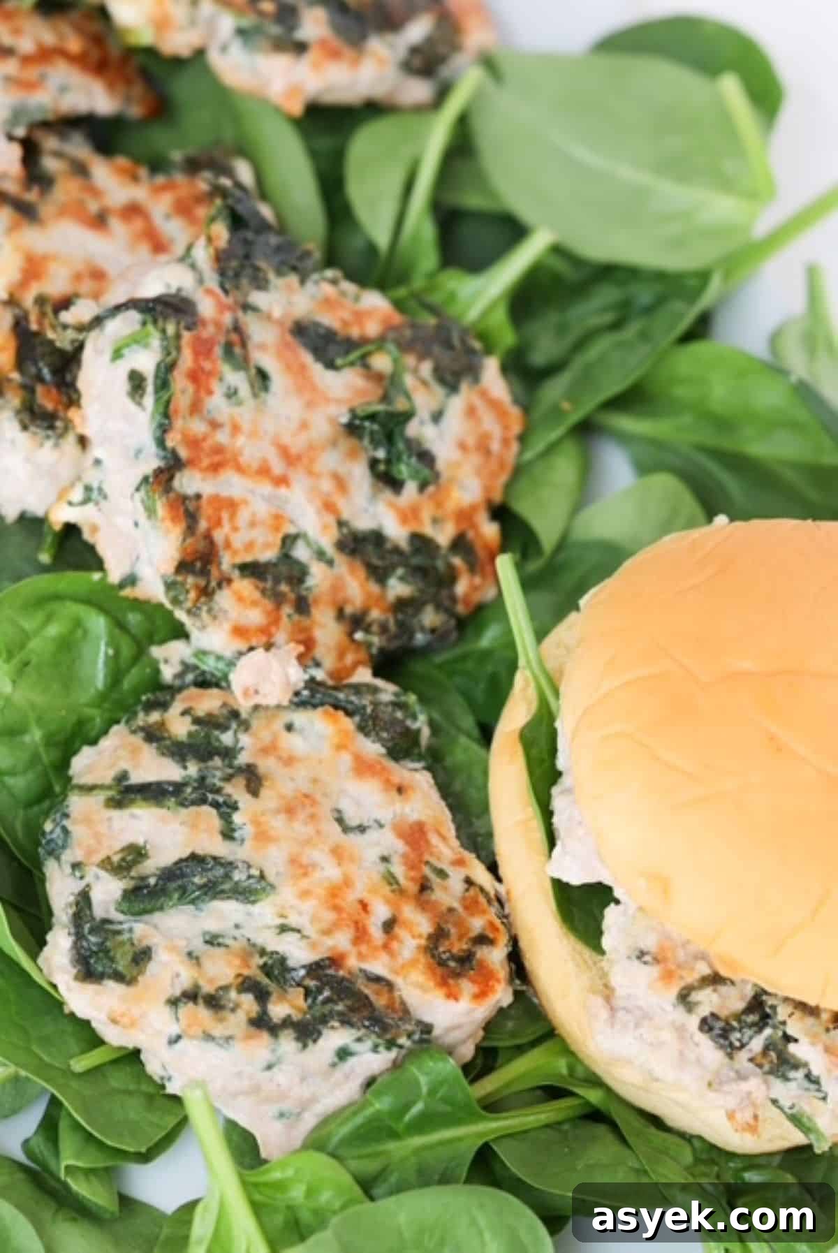 Turkey burgers with spinach and feta cheese on a bed of baby spinach and one burger in a burger roll.