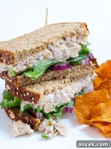 Two halves of a tuna and chickpea salad stacked with a toothpick through the center with a side of sweet potato chips.