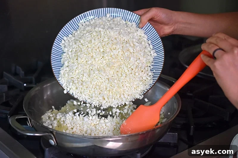 Whole30 Cauliflower Rice Recipes for Every Meal 5 A person pouring a plate of riced cauliflower into a large stainless steel skillet.