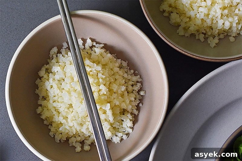 Whole30 Cauliflower Rice Recipes for Every Meal 7 An overhead shot of two bowls of simple cauliflower fried rice with a pair of silver chopsticks on top of one of the bowls.