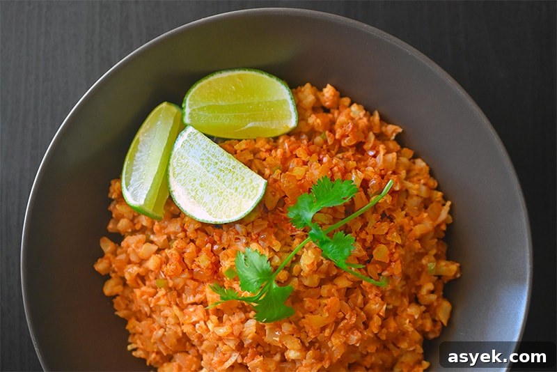 Whole30 Cauliflower Rice Recipes for Every Meal 8 An overhead shot of a bowl of Mexi-Cauli rice topped with a cilantro sprig and lime wedges.