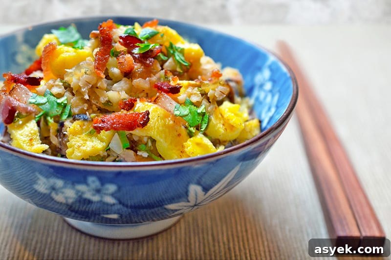 Whole30 Cauliflower Rice Recipes for Every Meal 9 A side view of Asian Cauliflower Fried Rice in a blue and white bowl with a pair of wooden chopsticks on the side.