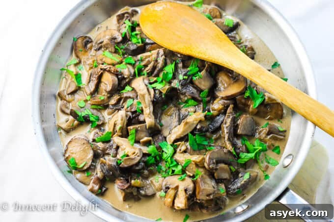 Creamy Mushroom Sauce with wide mushrooms in a pan with wooden spoon.