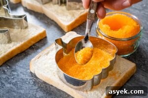 Sprinkling orange sugar with a spoon into a silver pumpkin cutter on a slice of white bread