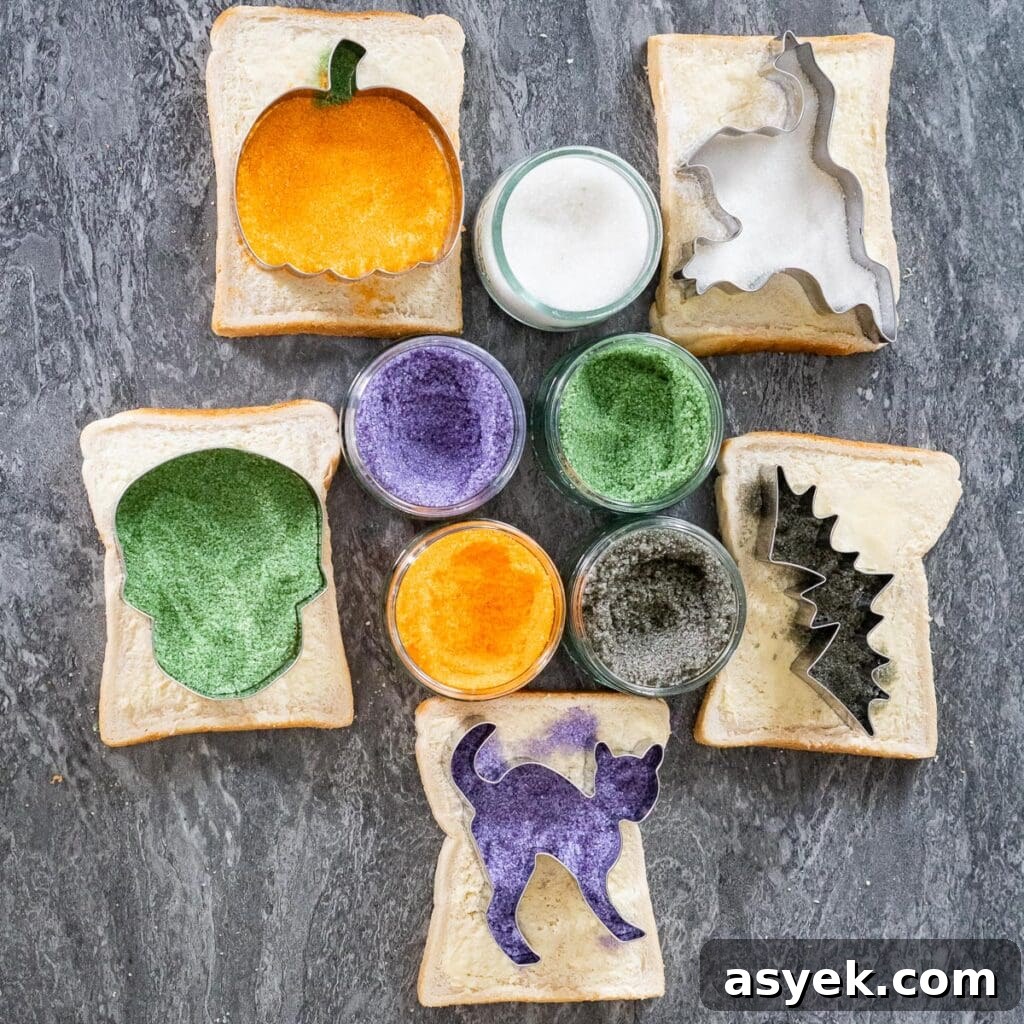 Five slices of buttered bread with each slice having a sugar coated Halloween characters pumpkin, Frankenstein, ghost, bat and cat and five glass ramekins with purple, green, orange, black and white sugar inside them
