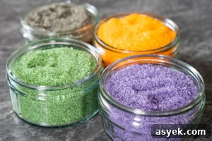 Four glass ramekins with green, orange, black and purple sugar inside them