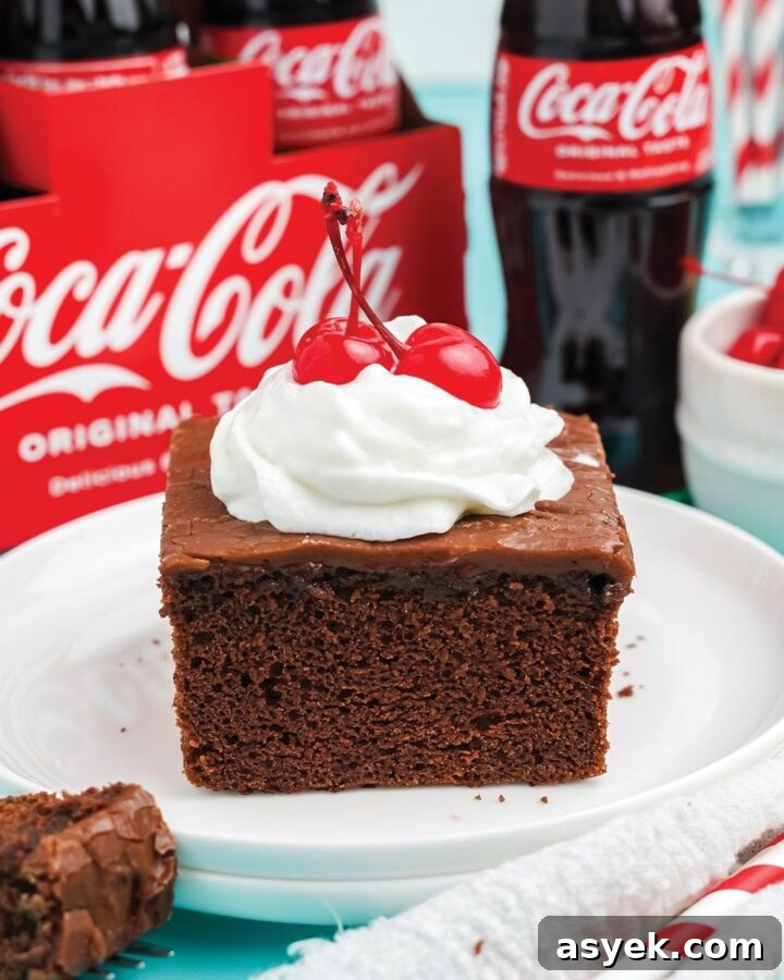 Slice of coca cola cake topped with whipped cream and a cherry.