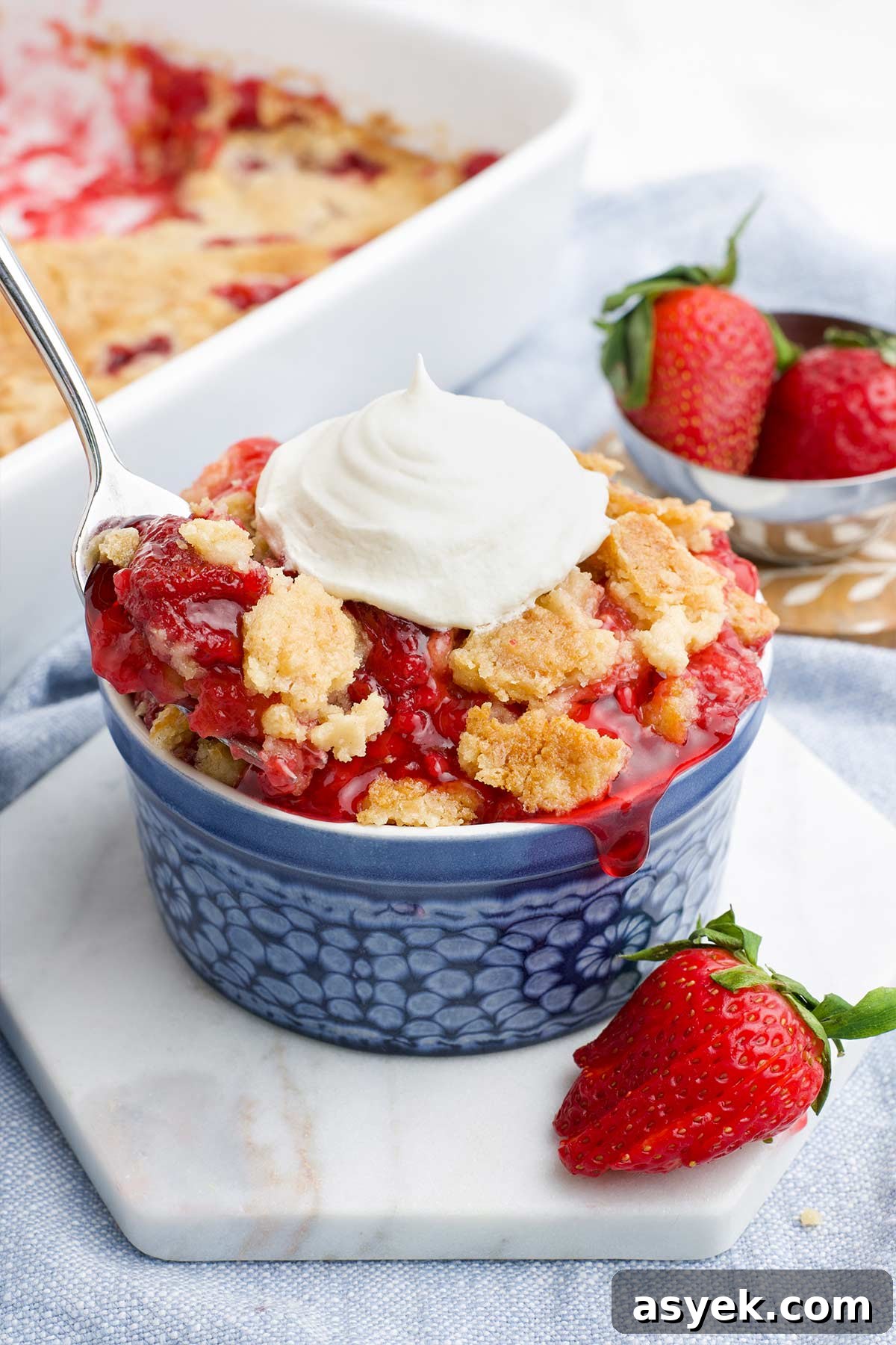 A little blue dessert bowl filled with strawberry dump cake and topped with whipped cream.