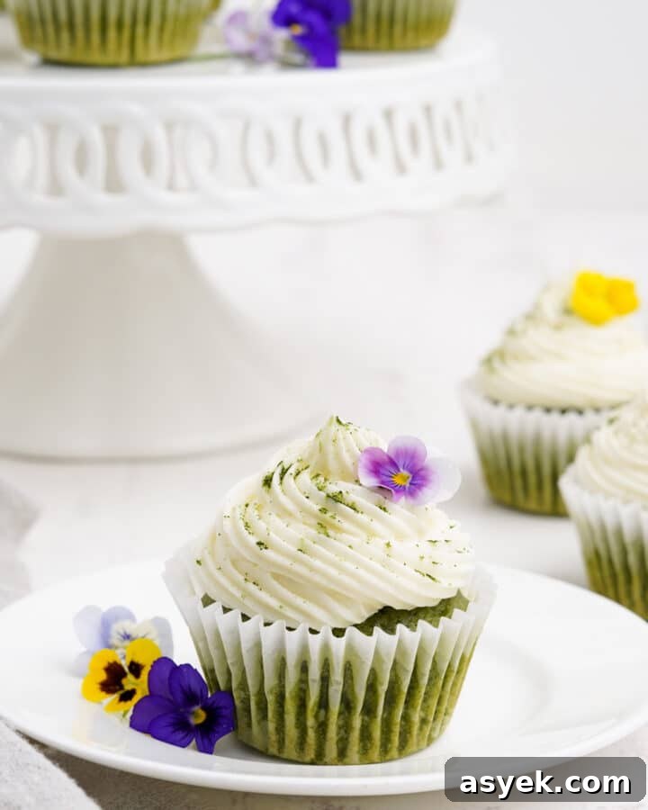 Matcha cupcake on a plate with flowers and more cupcakes in the background.