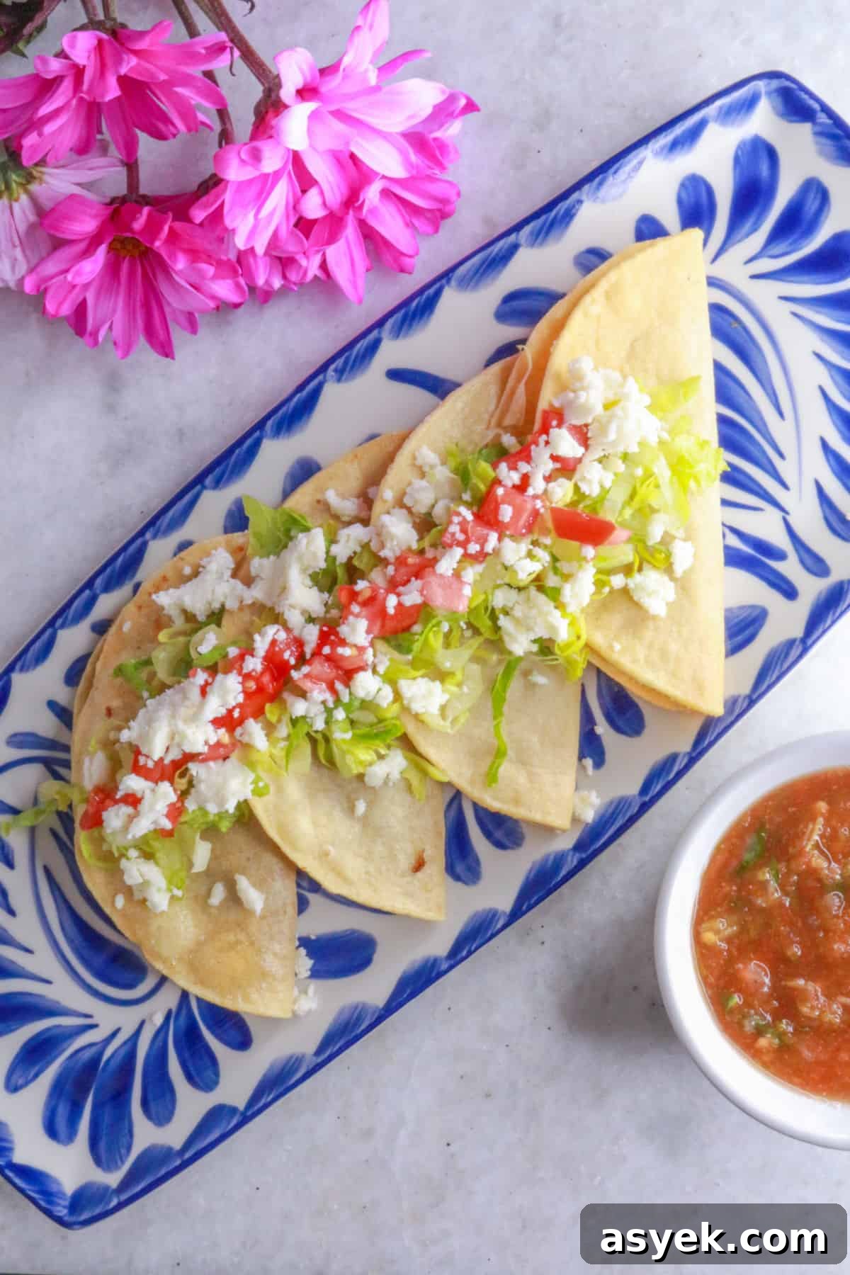 Crispy Mexican Bean Taco Recipe (Tacos Dorados) 2 Tacos dorados de frijoles in a row on a platter, topped with lettuce, tomatoes and queso fresco