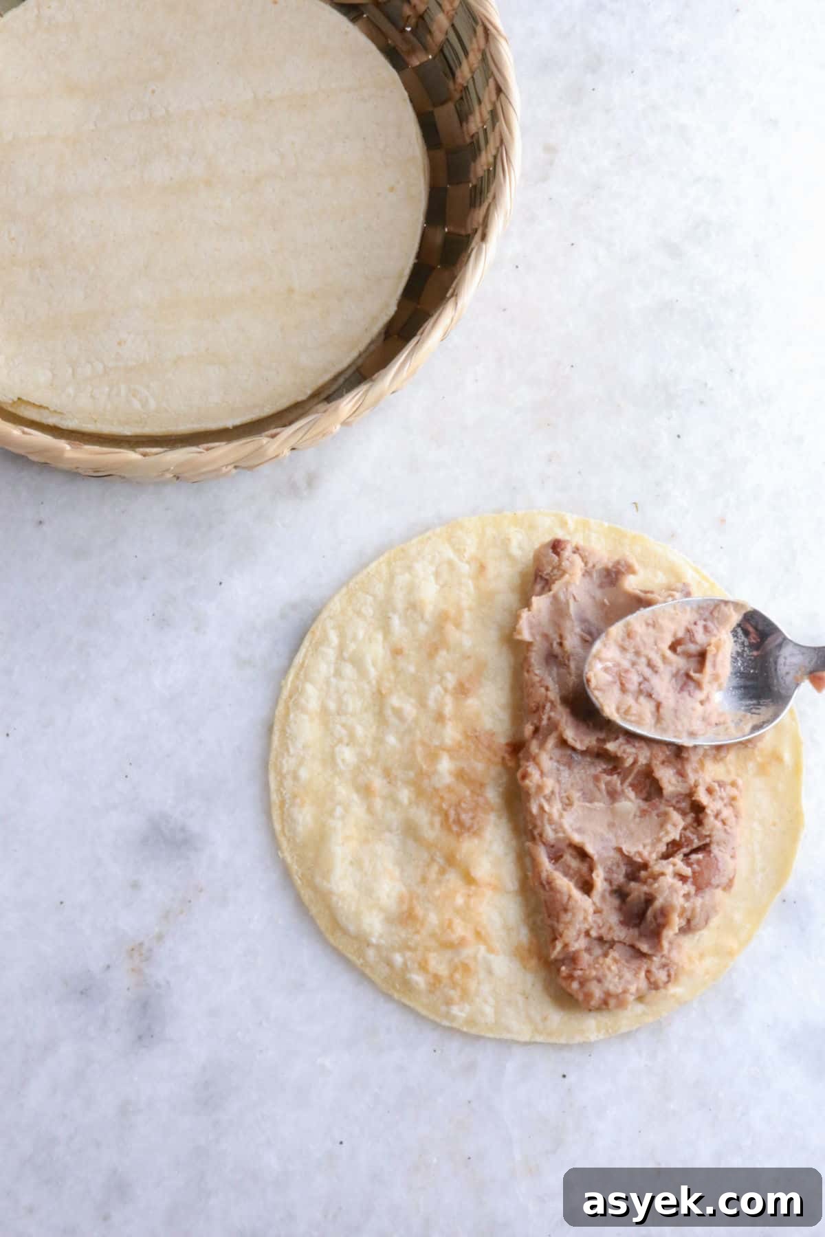 Crispy Mexican Bean Taco Recipe (Tacos Dorados) 5 Using a spoon to spread refried beans on a warm corn tortilla