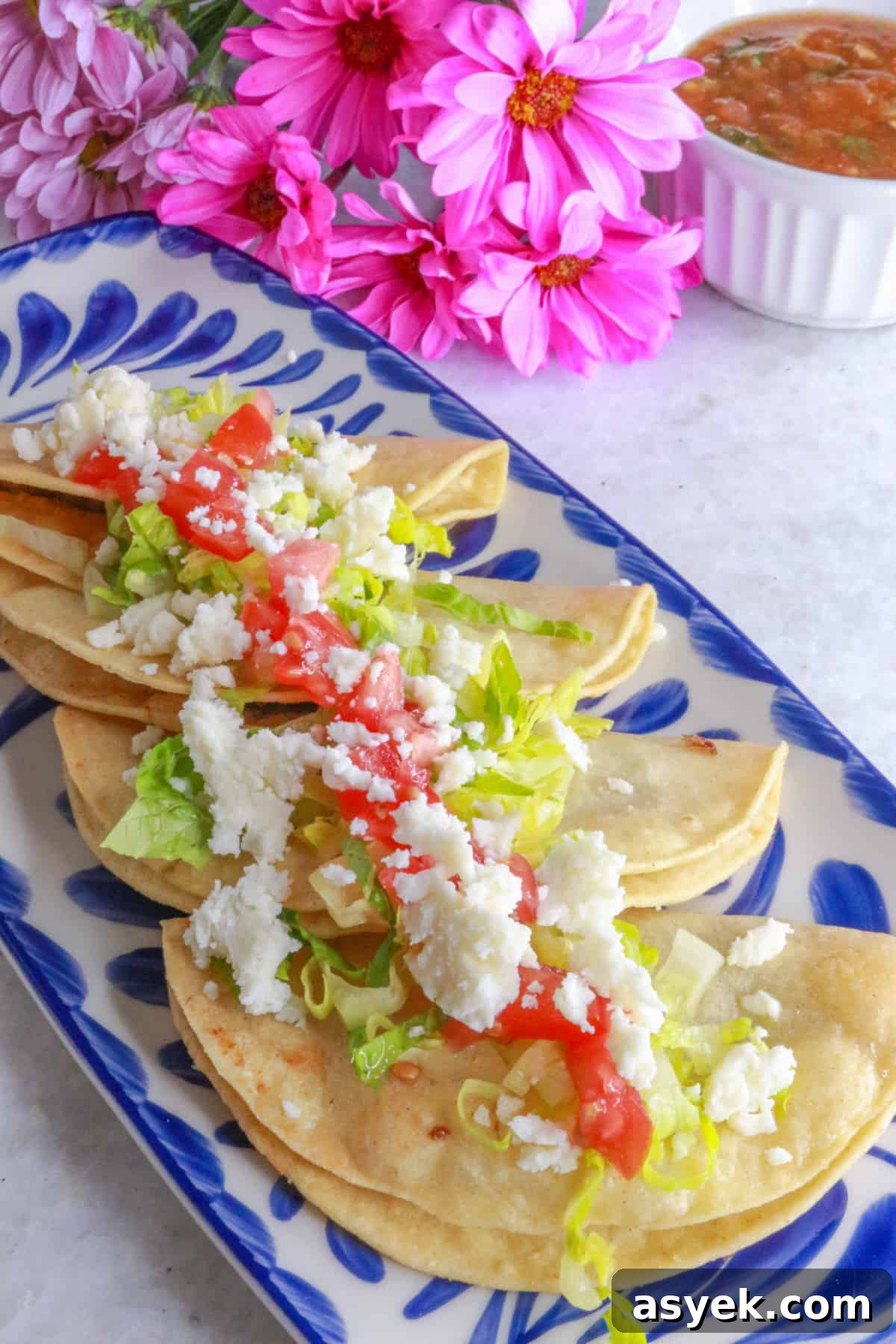 Crispy Mexican Bean Taco Recipe (Tacos Dorados) 9 Side view of Tacos dorados de frijoles in a row on a platter, topped with lettuce, tomatoes and queso fresco