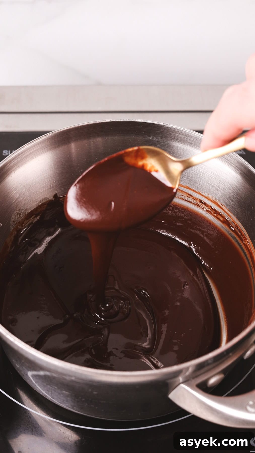 Chocolate melting in a small saucepan with a spoon showing off the smooth texture.