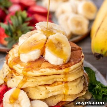 Stack of banana slices on a plate, banana slices on the stack and maple syrup pouring on top