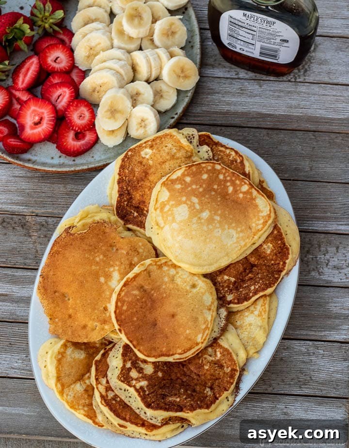 Platter of pancakes, plate of sliced bananas and strawberries on the side
