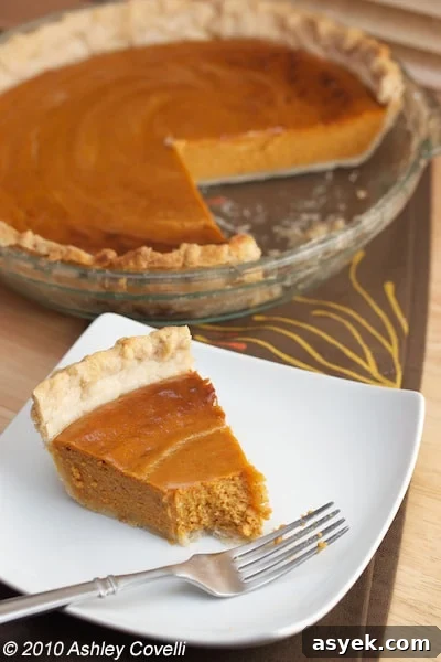 Pumpkin pie with a slice on a plate and a bite taken out of it.