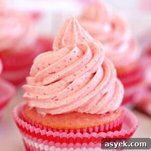 Close up of cupcake frosted with strawberry buttercream in a pink cupcake liner.