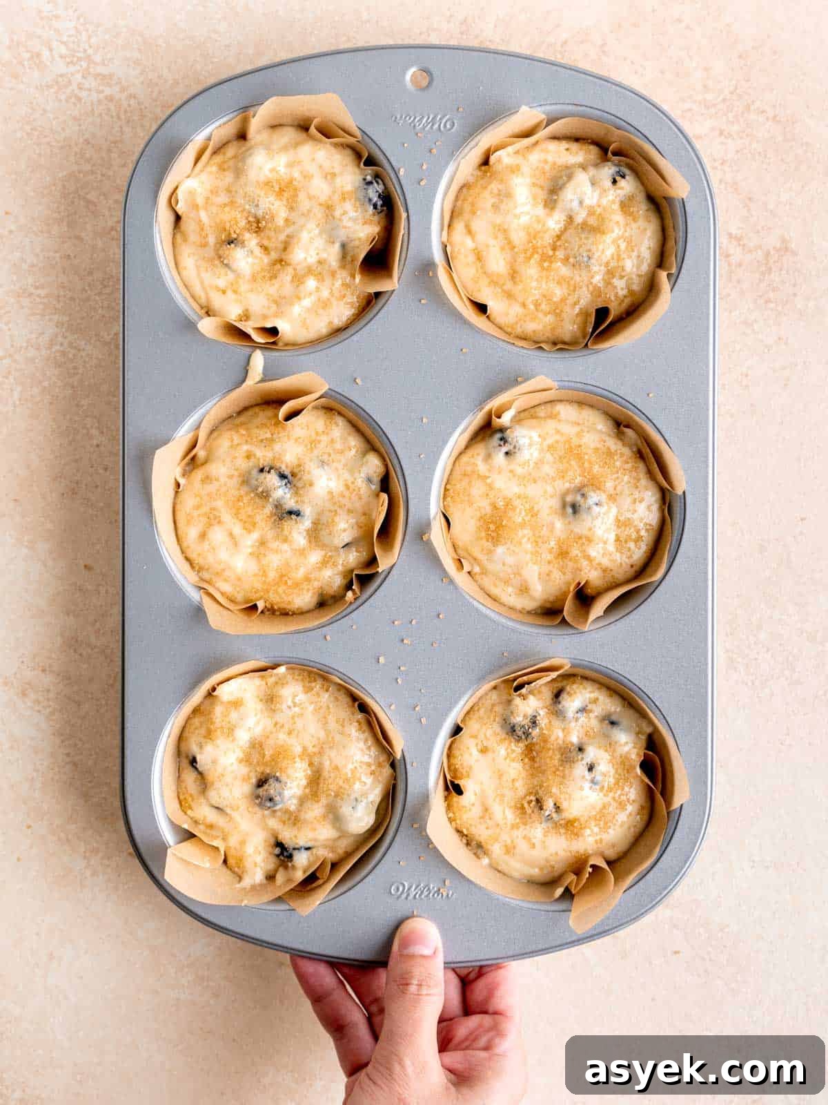 Blueberry sourdough discard muffin batter topped with demerara sugar in a muffin pan.