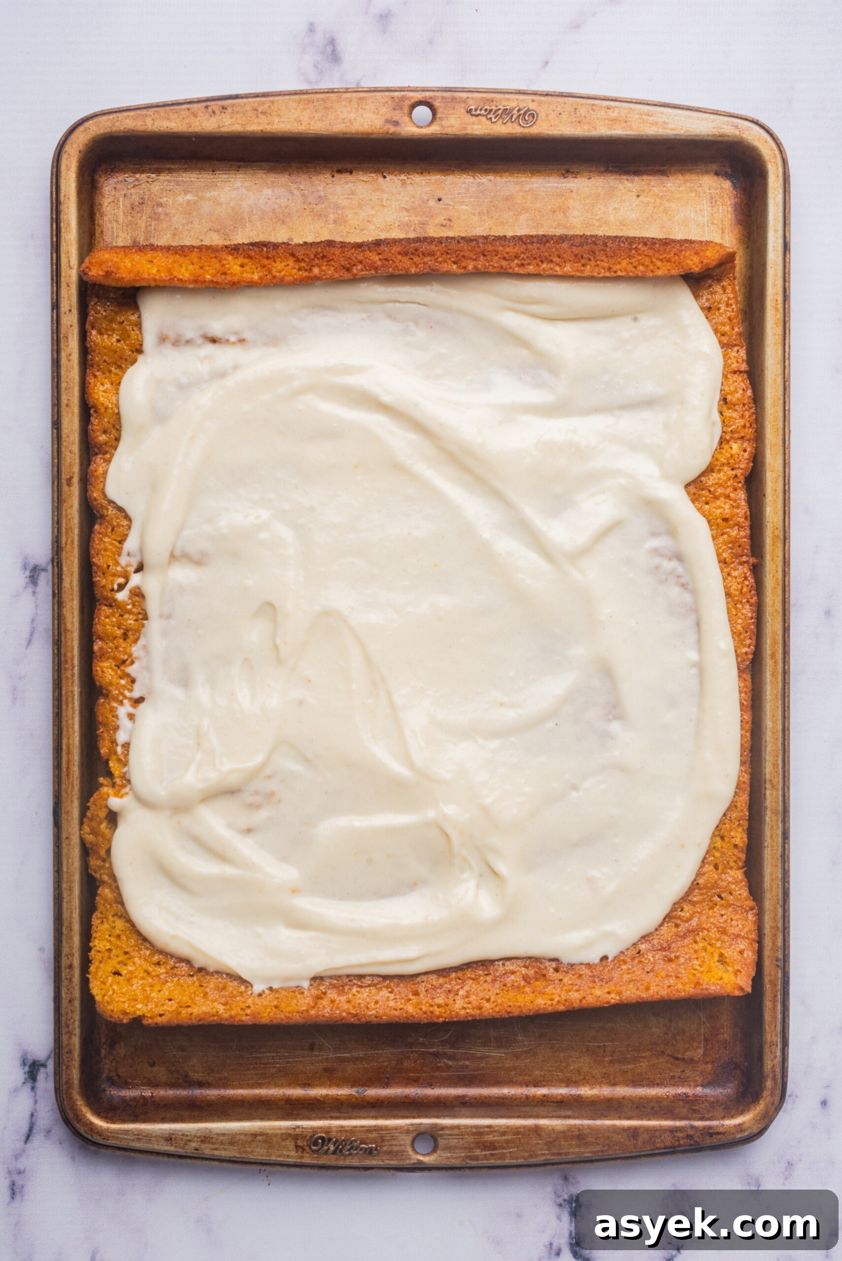 Baked pumpkin roll unrolled and covered with a layer of cream cheese filling on a baking tray.