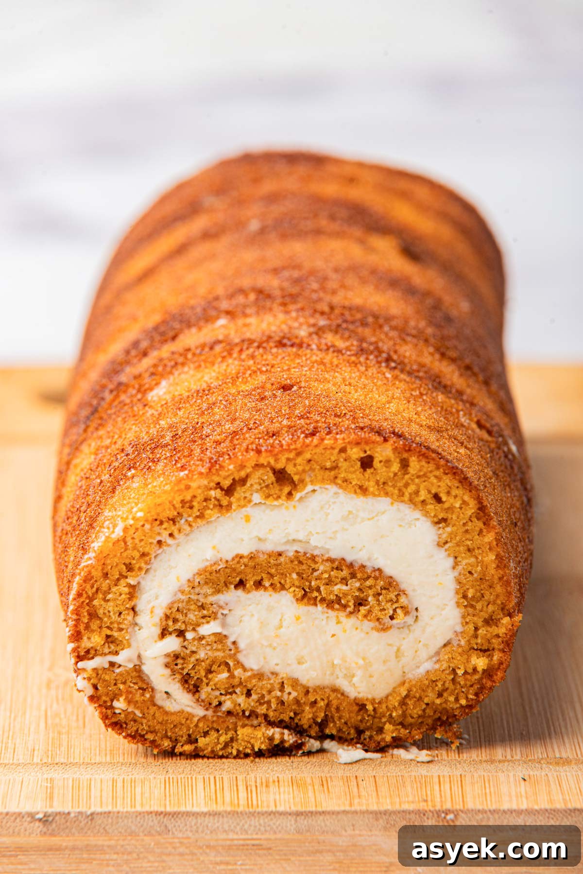 Pumpkin cake with cream cheese filling, showcasing the spiral pattern, placed on a wooden cutting board.