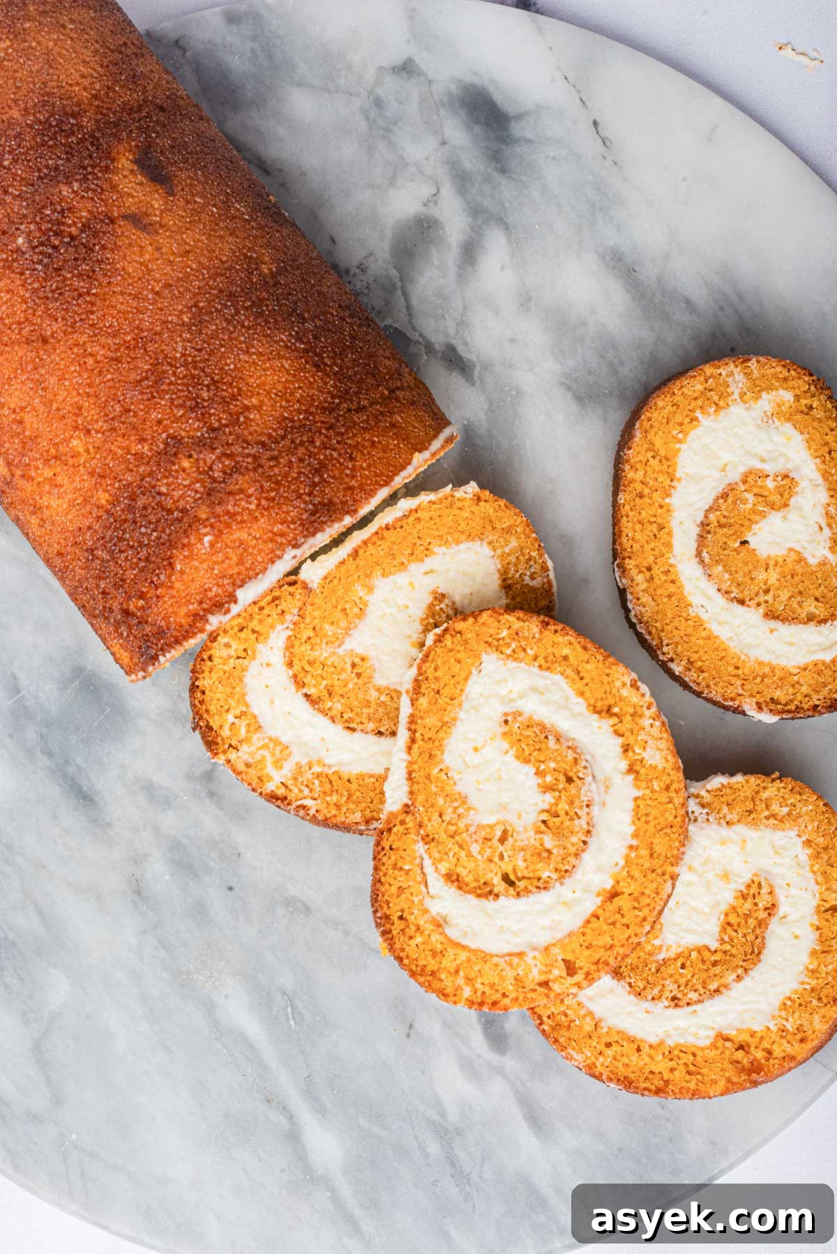 Top view of a roll cake with cream cheese filling partially sliced on a marble surface.