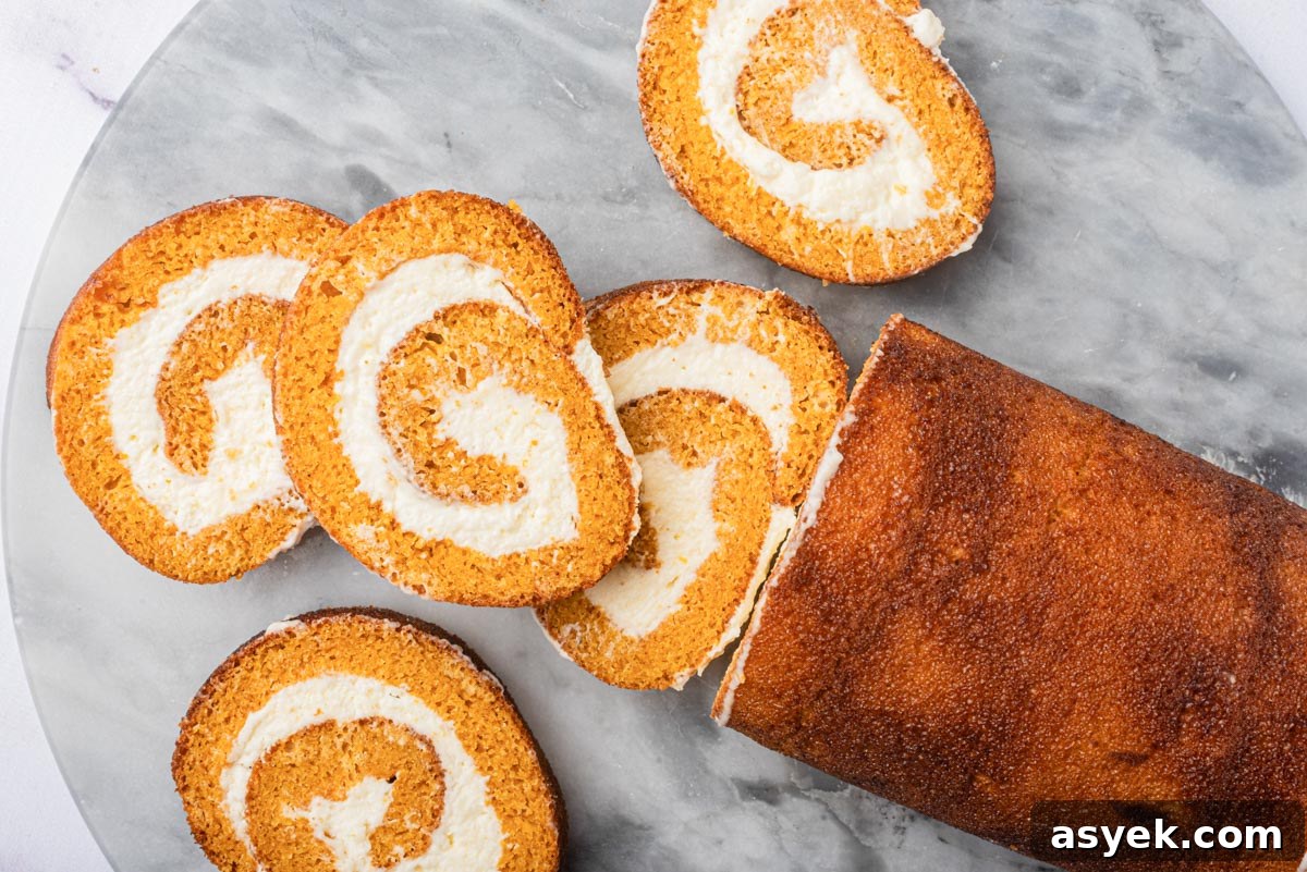 Slices of a cake roll with cream cheese filling spread out on a marble surface, showing the spiral pattern.
