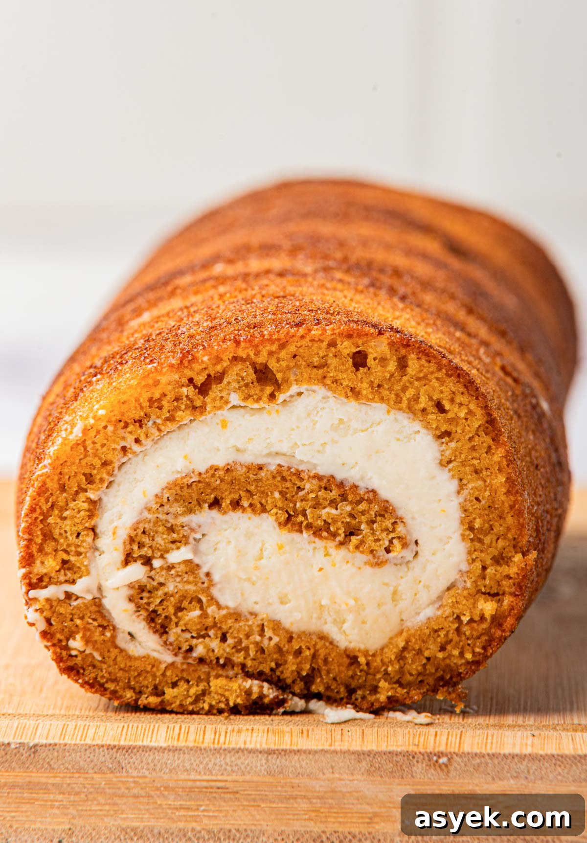 Front view of a pumpkin cake with cream cheese filling, showing the rolled layers on a wooden cutting board.