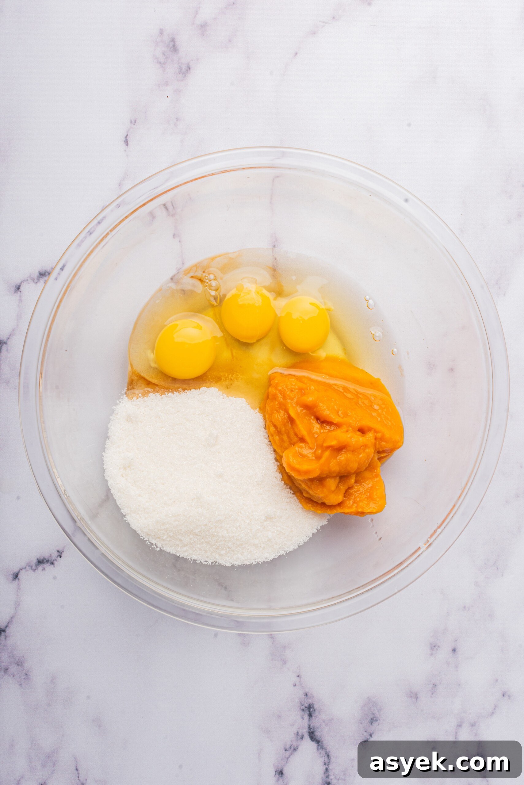 Ingredients for the pumpkin log in a glass bowl, including eggs, granulated sugar, and pumpkin puree, before being mixed.