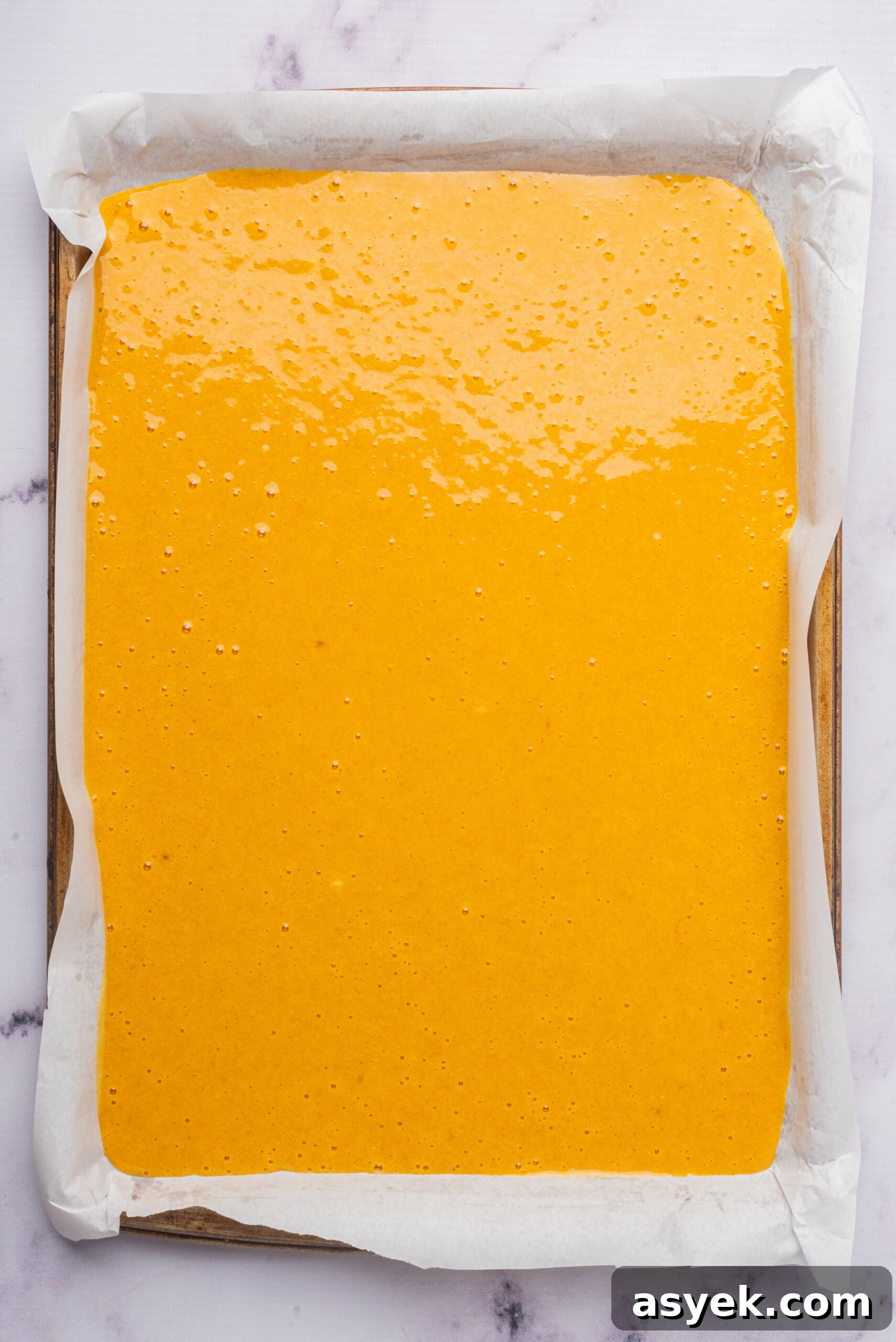Batter spread evenly in a parchment-lined baking pan, ready to be baked.