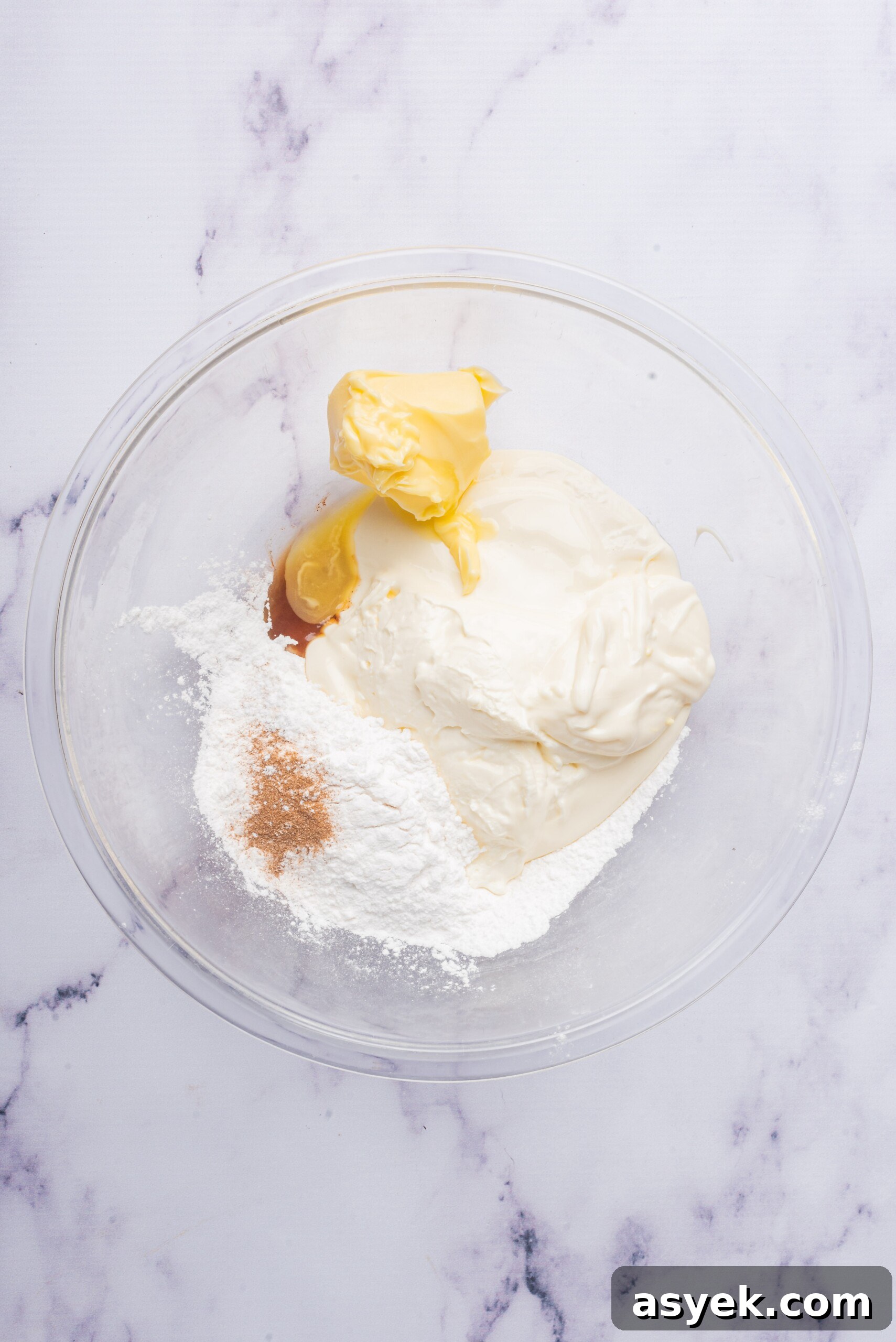Ingredients for the cream cheese filling in a glass bowl, including cream cheese, powdered sugar, butter, and vanilla extract, before being mixed.