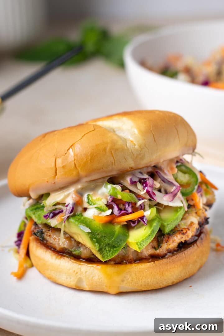 close up view of a ground chicken burger topped with avocado, slaw and creamy spicy sauce