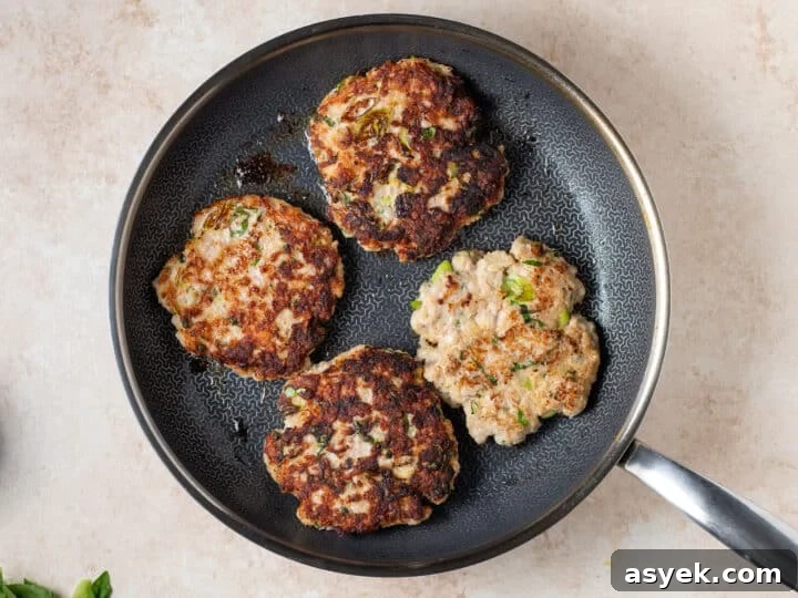 chicken patties cooking in a skillet with a golden brown crust
