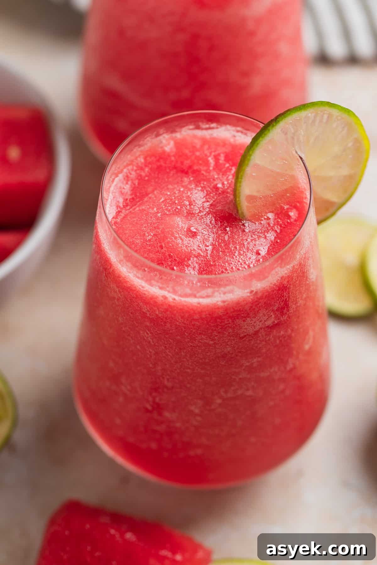 Watermelon frose in glasses with lime slice and watermelon slices beside the glasses.