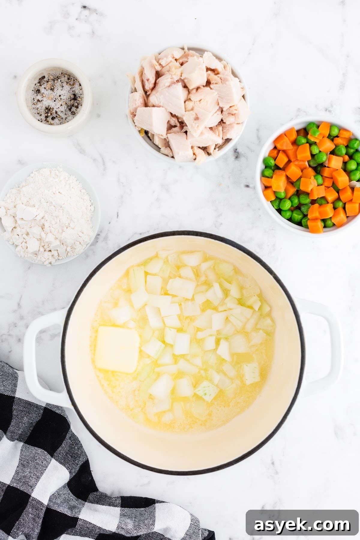 Onions in melted butter in a pot next to other pot pie ingredients.