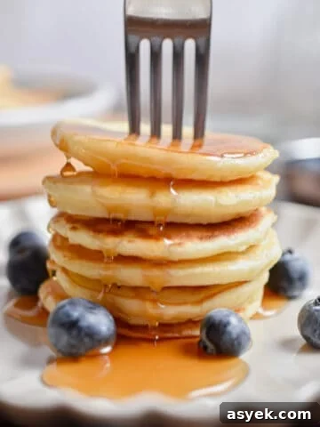 A fork is in a stack of silver dollar pancakes with maple syrup.