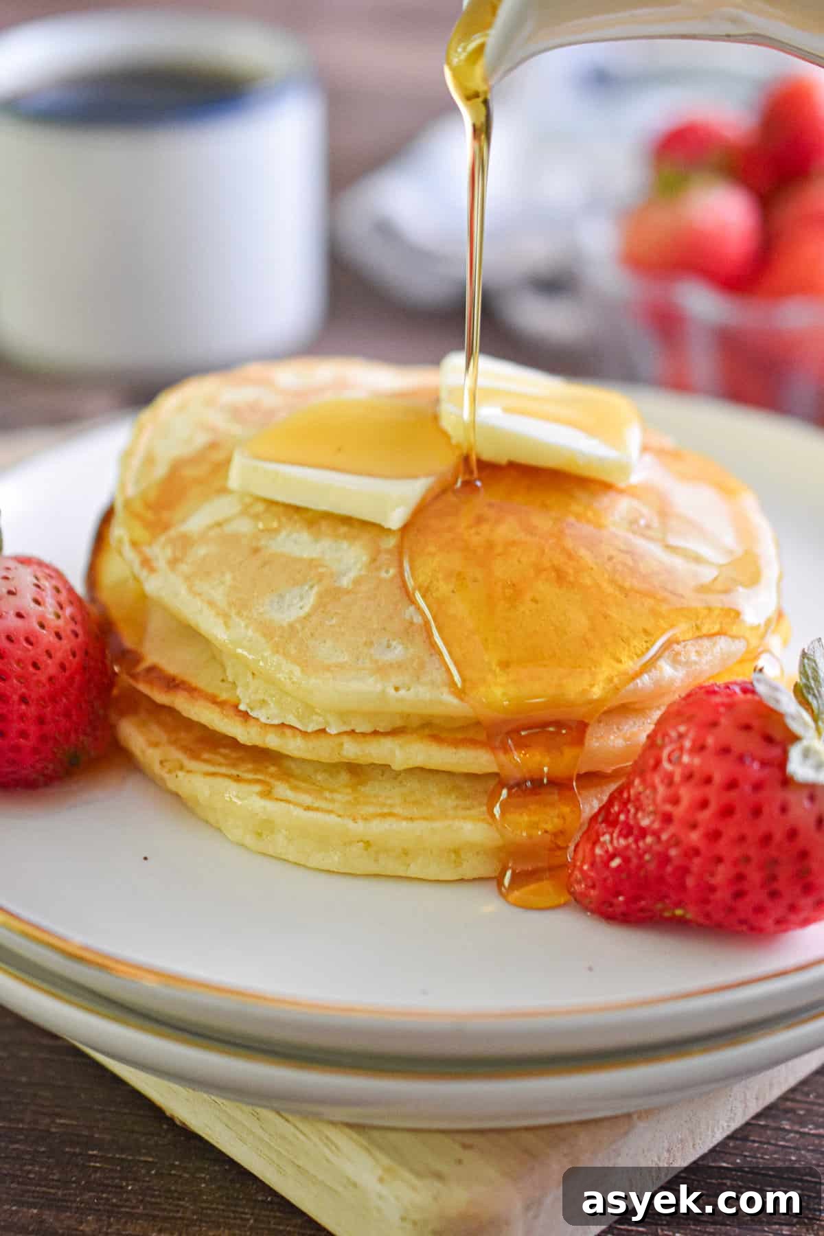 Maple syrup is being poured over a stack of pancakes.