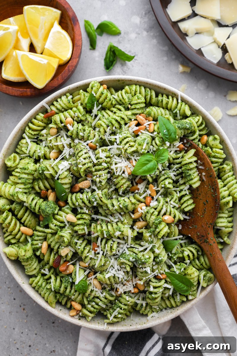 Kale Pesto Pasta with Homemade Pesto Sauce 6 A serving bowl filled with kale pesto pasta surrounded by a bowl of lemon wedges, fresh basil leaves and shaved parmesan