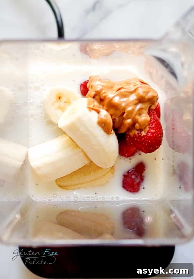 Creamy Strawberry Banana Peanut Butter Smoothie Recipe 5 Top down view of a blender filled with milk, bananas, peanut butter, and strawberries.