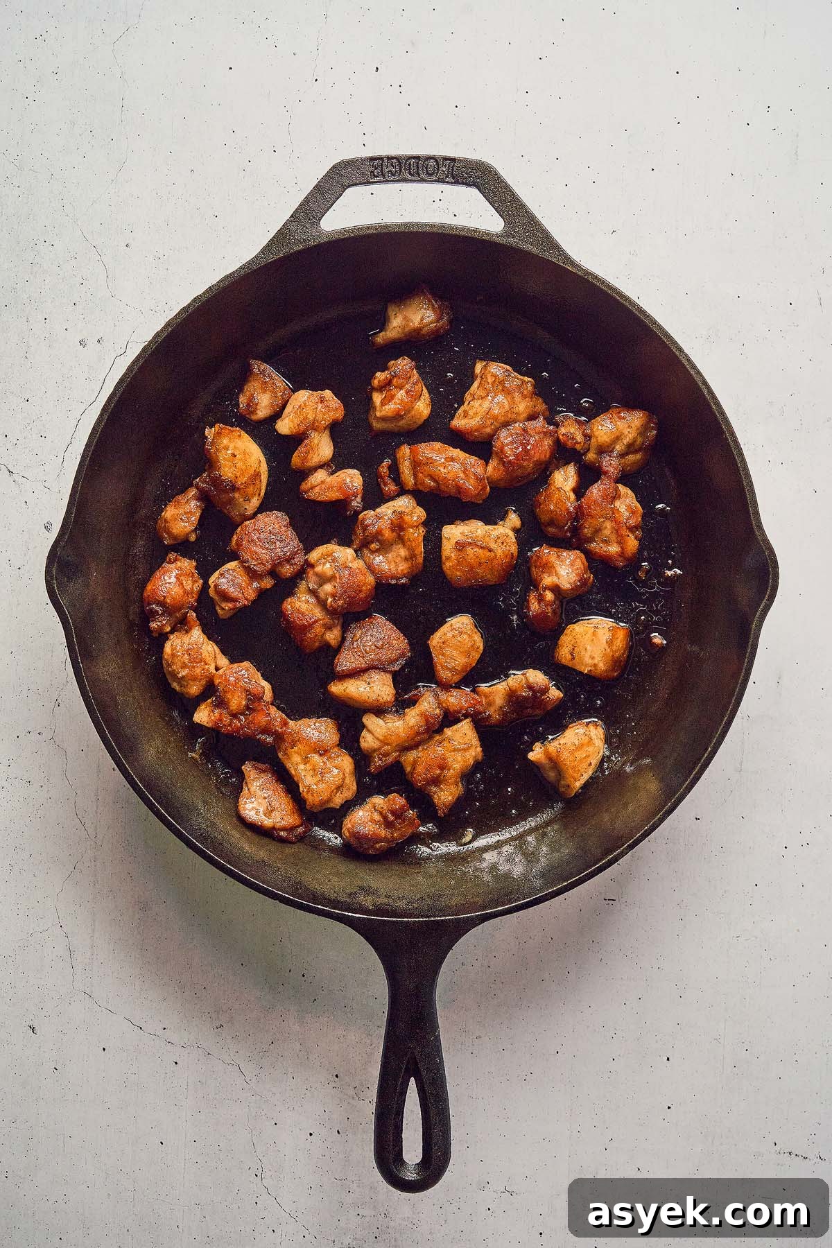 Chunks of browned meat in a black cast-iron skillet on a light surface, infused with the aromatic essence of five spice, bringing the allure of a chicken stir fry to life.
