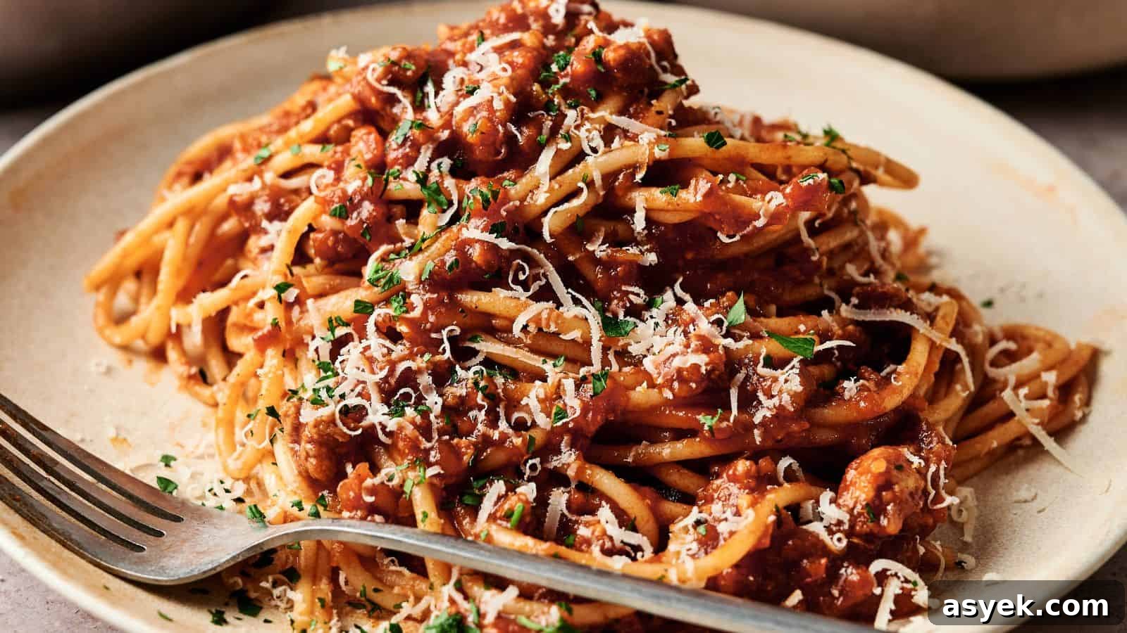 A plate of spaghetti topped with meat sauce, grated cheese, and chopped herbs, with a fork resting on the plate.