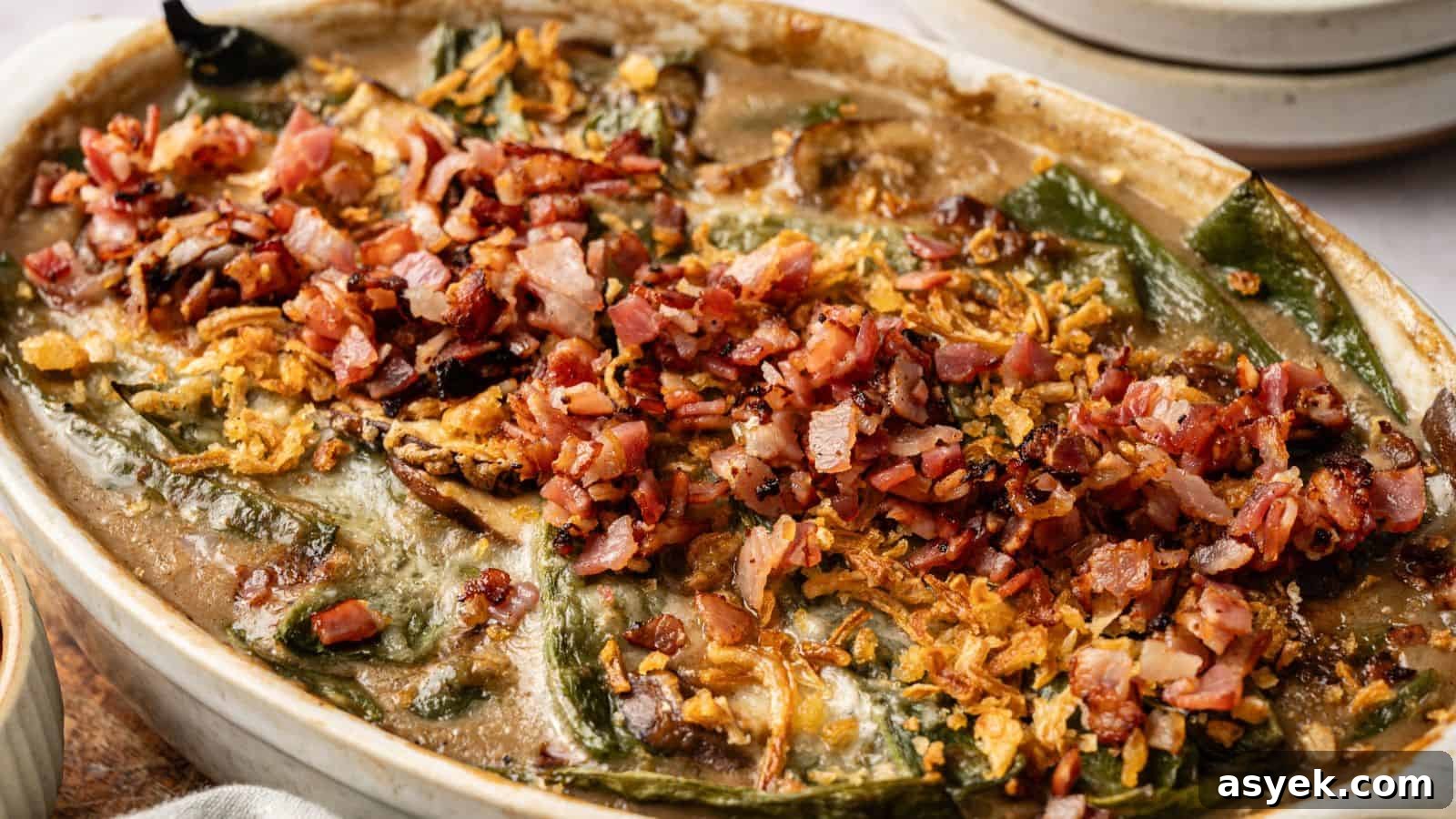 A baked casserole topped with chopped bacon, crispy onions, and melted cheese, featuring visible green peppers and a creamy sauce.