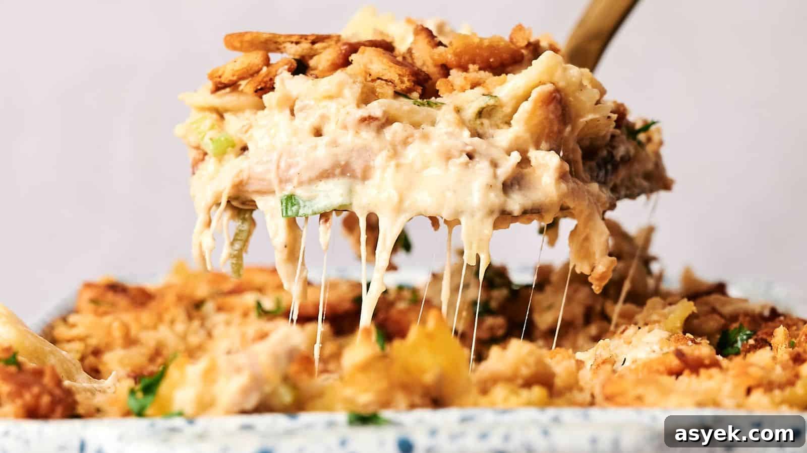 A serving spoon lifts a portion of creamy, baked casserole with a crunchy topping, revealing melted cheese.