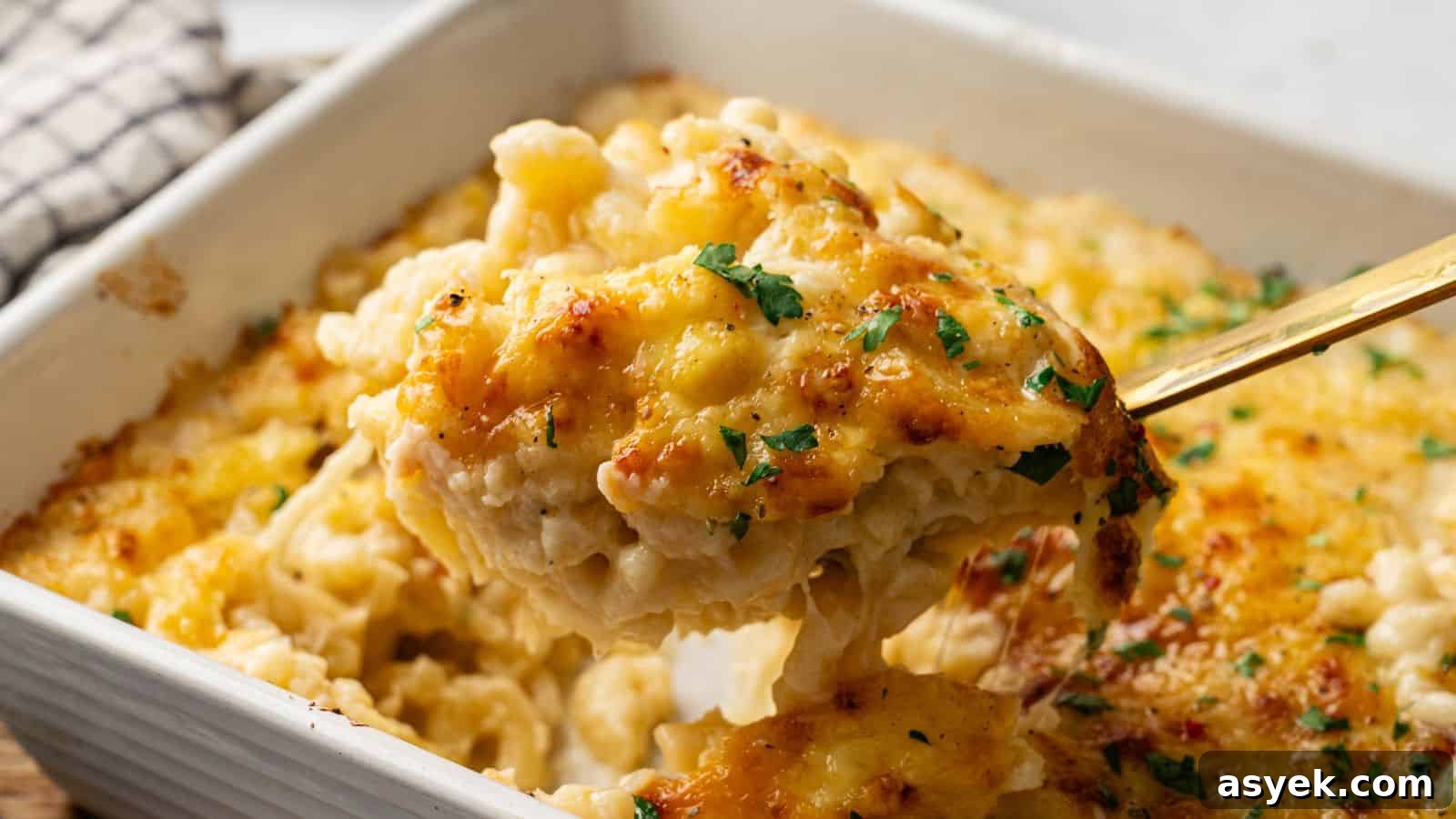 A close-up of a serving of baked macaroni and cheese being lifted from a casserole dish, topped with melted cheese and garnished with chopped herbs.