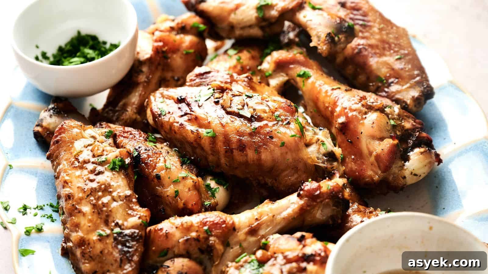 A plate of cooked chicken wings garnished with chopped herbs, accompanied by two small bowls of dipping sauces.